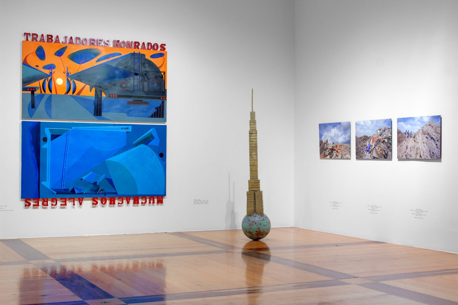 Sala con fotografías enmarcadas, una pintura mural fragmentada y un retrato, junto a una estructura de madera