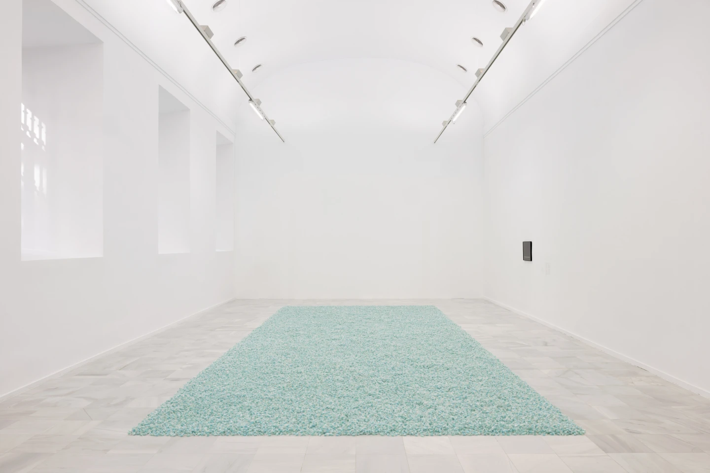 Guirnalda de luces de Felix Gonzalez-Torres suspendida en una sala del Reina Sofía, con un friso verde y una pila de papel azul en el suelo